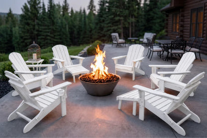Six white Adirondack-style outdoor chairs arranged around a fire pit on a concrete patio, with a cabin, trees, and patio furniture visible in the background at dusk.