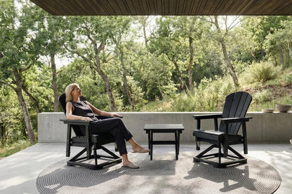 Woman sitting on a black chair in a garden setting with trees and a stone wall.