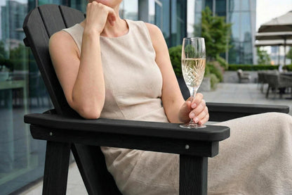 Woman sitting in a black Adirondack chair holding a glass of champagne with a cityscape background.