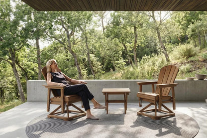 Woman sitting on a brown chair in a serene outdoor setting with trees and a clear sky.