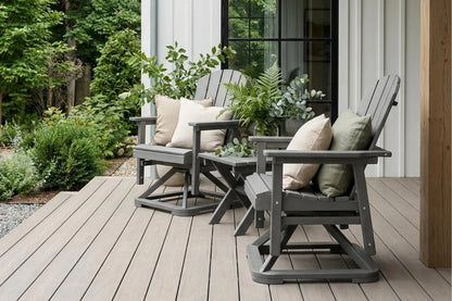 Two gray Adirondack chairs with cushions on a wooden deck surrounded by greenery.