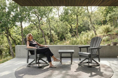 Woman sitting on a chair in a garden setting with trees and a clear sky.