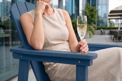 Woman sitting in a navy blue chair holding a glass of champagne with a blurred outdoor background