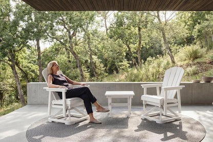 Woman sitting on a white chair in a serene outdoor setting with trees and a clear sky.