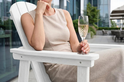 Woman sitting in a white chair outdoors, holding a glass of champagne.