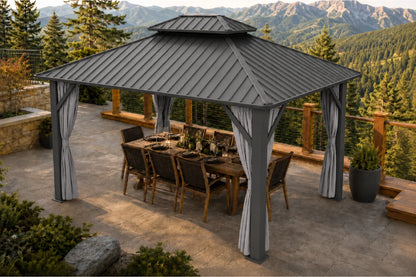 A dark gray hardtop gazebo with netting and curtains, sheltering a wooden dining table and chairs. The gazebo is situated on a stone patio with a scenic mountain and pine forest background.