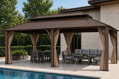 A brown hardtop gazebo with netting and curtains, furnished with a dining set and a gray outdoor sofa, situated next to a swimming pool on a paved patio in front of a modern house.