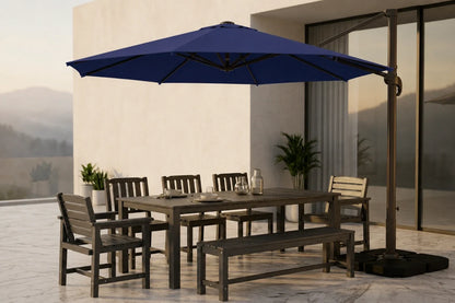 Outdoor patio dining set with a rectangular wooden table, matching bench, and six chairs under a large navy blue cantilever umbrella, staged on a tiled patio in front of a modern building.