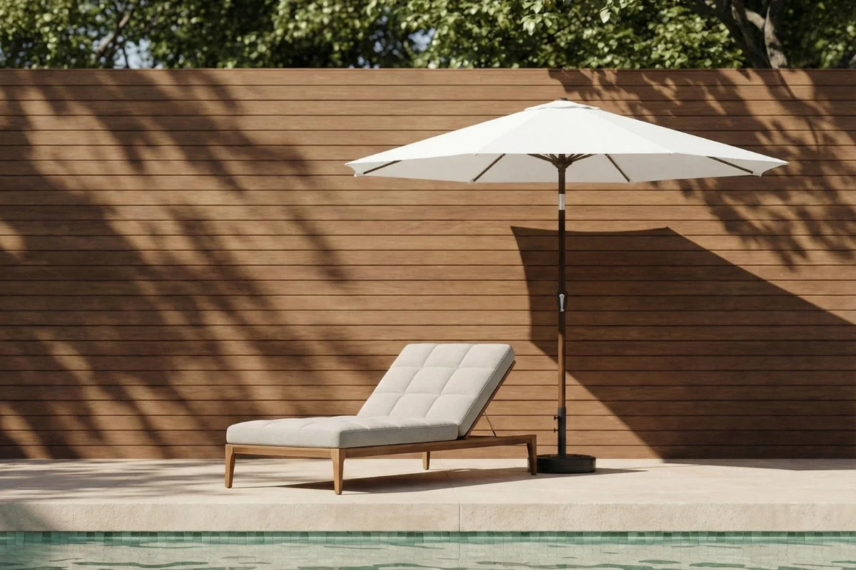 Chaise lounge with a white umbrella by a poolside against a wooden wall.