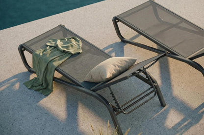 Two lounge chairs with a green towel and pillow by a poolside.