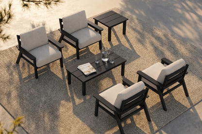 A 6-piece outdoor patio furniture set arranged on a textured beige rug. The set includes 4 black-framed armchairs with creamy white cushions, a matching black coffee table, a smaller black side table.