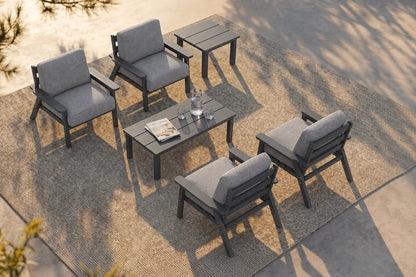 A 6-piece outdoor patio furniture set including four gray cushioned armchairs, one matching rectangular coffee table, and one matching side table, arranged on a textured beige rug over a concrete patio.