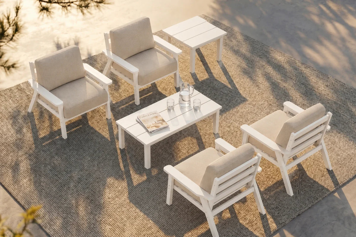A 6-piece outdoor patio conversation set with white frames and creamy white cushions, one matching rectangular coffee table, and one matching side table arranged on a textured gray rug.
