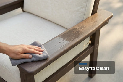 A close-up of a hand wiping down a brown outdoor chair armrest with a gray cloth. The chair has creamy white fabric cushions.