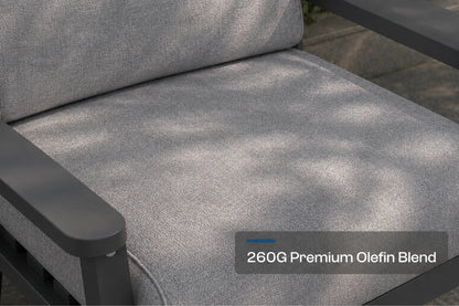Close-up of a gray outdoor chair cushion with a dark gray frame, showing dappled sunlight and shadow patterns on the fabric. A text overlay reads '260G Premium Olefin Blend'.