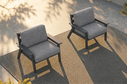 Two modern outdoor armchairs with gray textured cushions and dark gray frames, positioned on a concrete patio with long shadows under warm sunlight.