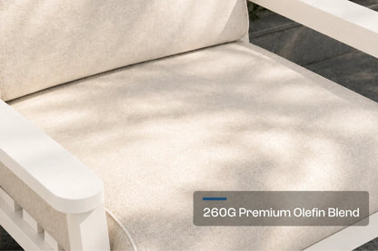 Close-up of a creamy white outdoor chair cushion with a white frame, showing dappled sunlight and a text overlay that reads '260G Premium Olefin Blend'.