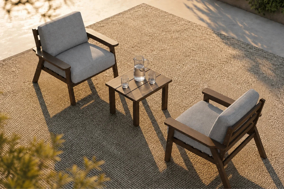 Two outdoor armchairs with gray cushions and brown frames arranged around a small square side table on a woven rug, photographed from above in a patio setting.