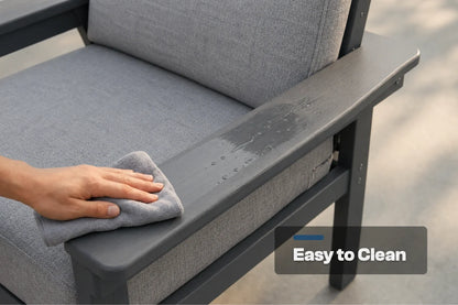 A close-up of a person's hand wiping down the armrest of a gray outdoor patio chair with a gray cloth. The chair has a dark gray frame and textured gray fabric cushions.